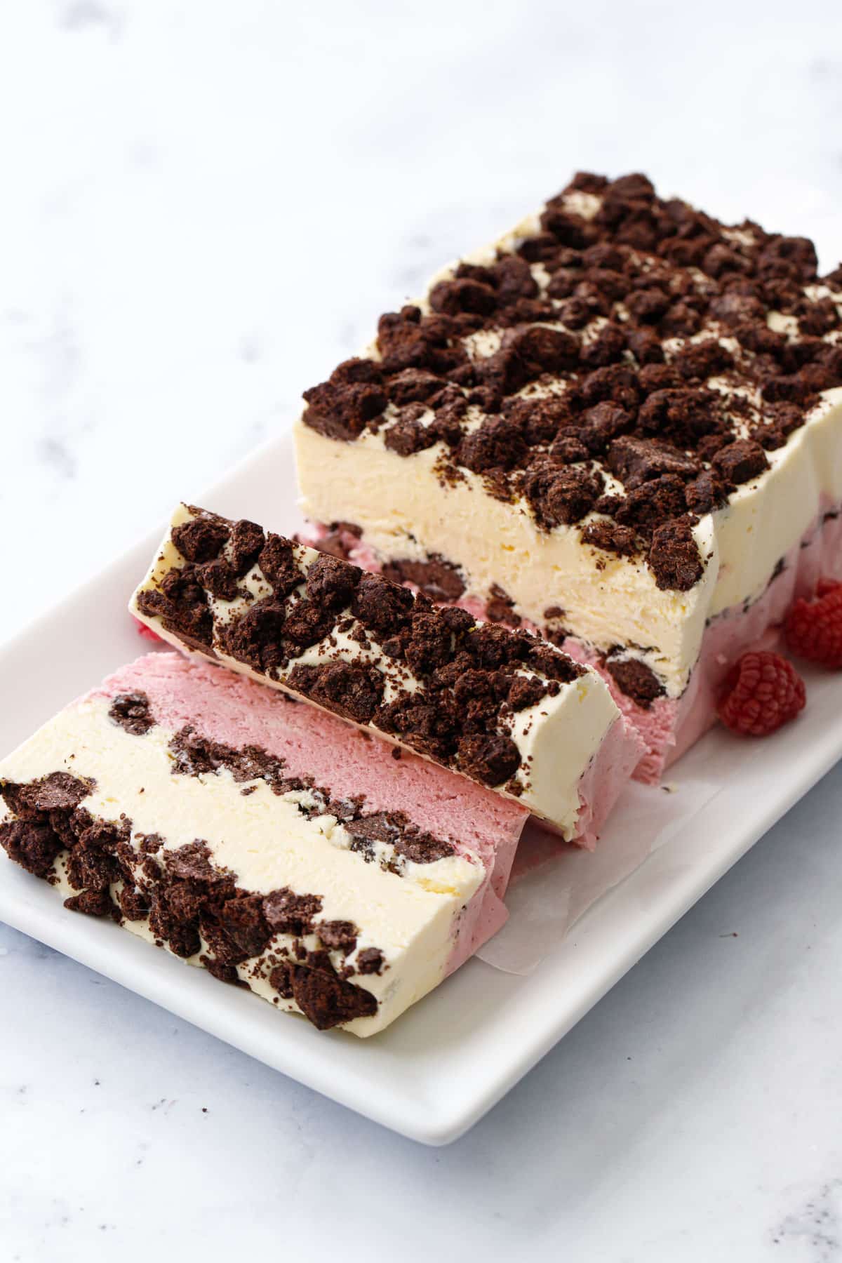 Frozen loaf of Raspberry & Passionfruit Semifreddo with Chocolate Crumbs in between and on top, on a white square plate, two slices laying on their sides.