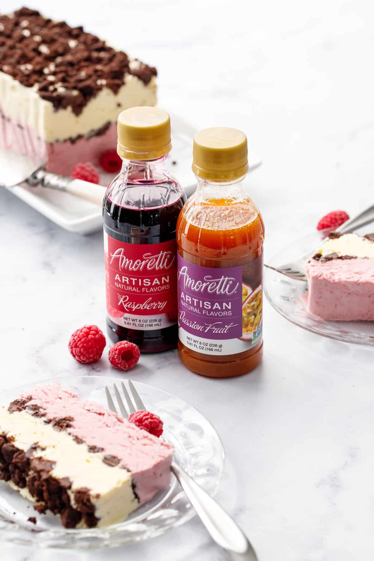 Two bottles of Amoretti Artisan flavors, Passionfruit and Raspberry, along with a few plates with slices of raspberry passionfruit semifreddo, and the rest of the frozen loaf in the background.