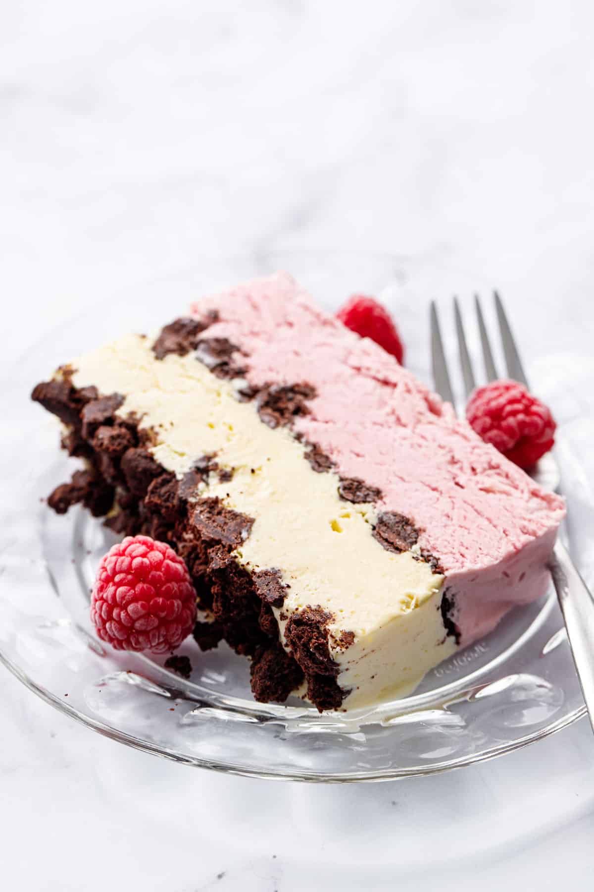 Closeup texture shot of a slice of Raspberry & Passionfruit Semifreddo with Chocolate Crumbs on a glass plate with fork and frozen raspberries.