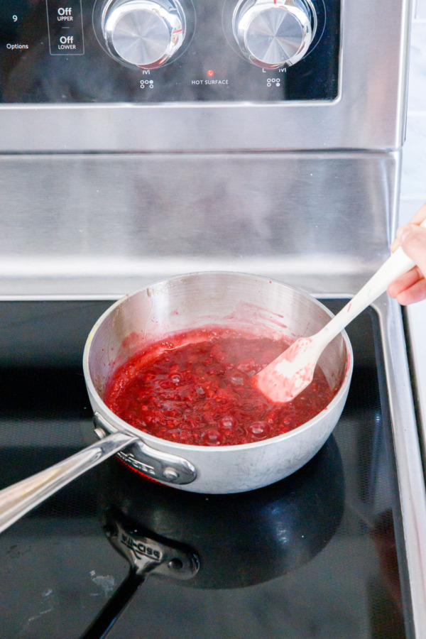 Simmering raspberries, sugar and corn syrup in a small saucepan on the stovetop.