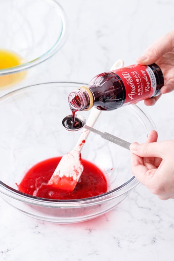 Measuring 1 teaspoon of Amoretti Natural Artisan Raspberry Flavor into bowl with strained raspberry mixture.