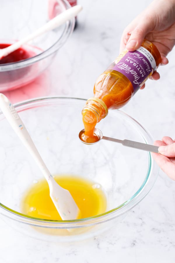 Measuring 1 teaspoon of Amoretti Natural Artisan Passionfruit Flavor into glass mixing bowl with cooked passionfruit mixture.