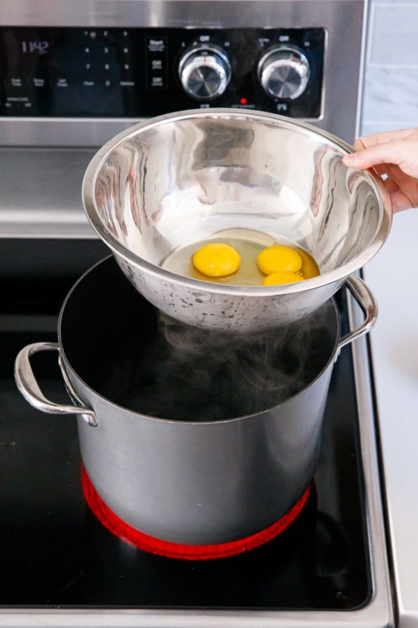 Placing a stainless steel mixing bowl on top of a saucepan with simmering water inside.