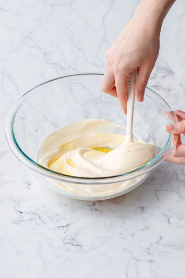 Folding fluffy whipped egg/sugar mixture into passionfruit base with a spatula in a glass mixing bowl.