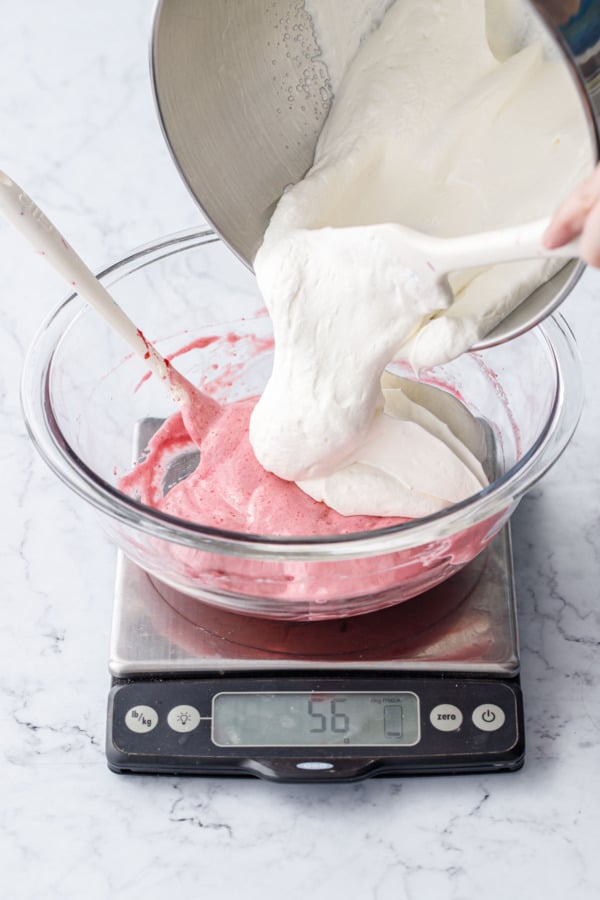 Spooning cream whipped to soft peaks into mixing bowl with raspberry base mixture.