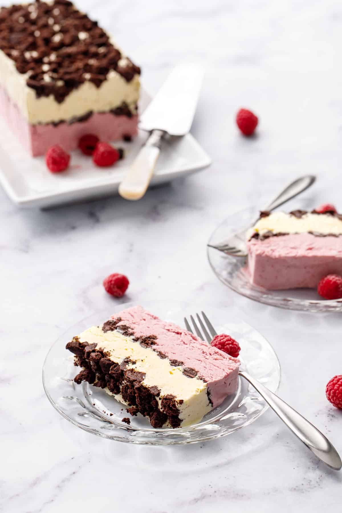 Slices of Raspberry & Passionfruit Semifreddo with Chocolate Crumbs on glass plates, rest of the frozen loaf in the background with a few frozen raspberries scattered around.