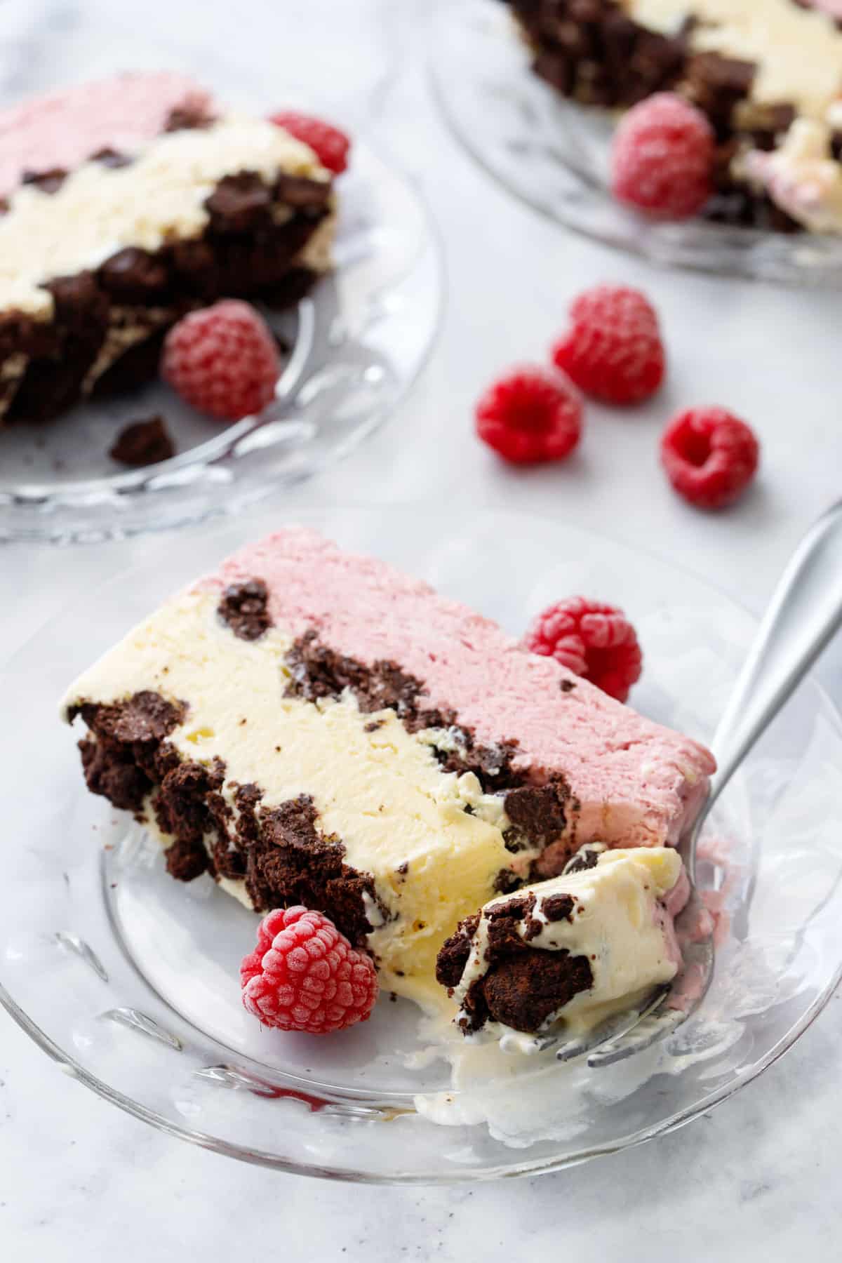 Slices of Raspberry & Passionfruit Semifreddo with Chocolate Crumbs on glass plates, front slice with a forkful taken out of it to show the creamy melty texture.