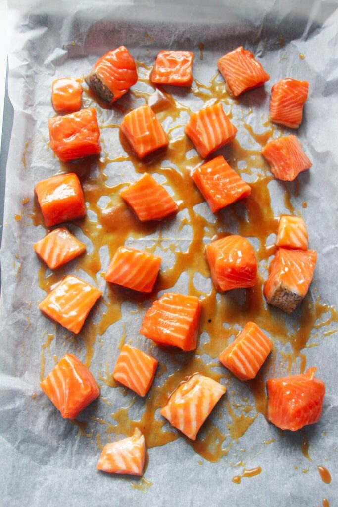 Cubed salmon tossed in miso honey marinade on a lined oven tray.