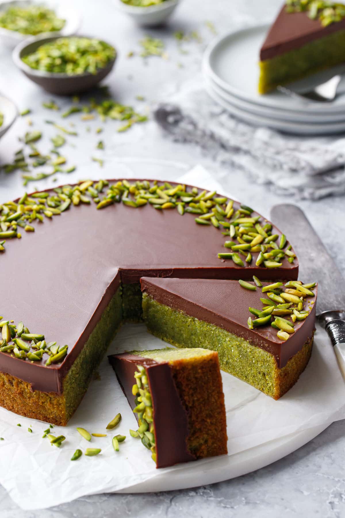 Flourless Pistachio Cake with Chocolate Ganache on a gray background, two slices cut to show the bright green color inside.
