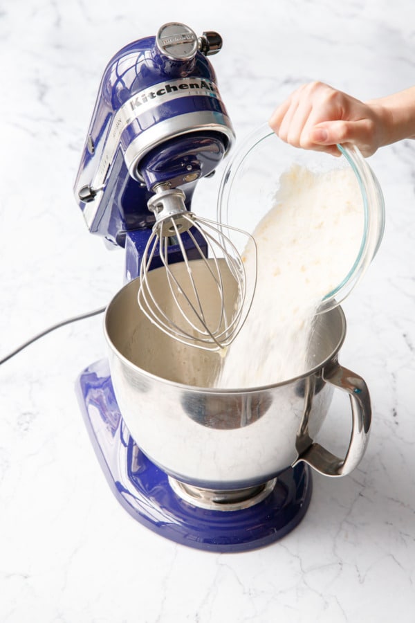 Pouring orange zest-infused sugar into a the bowl of a blue stand mixer.