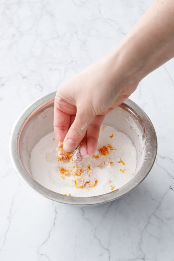 Rubbing orange zest into a small bowl of granulated sugar.