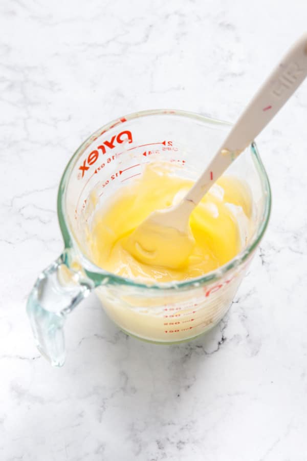 Partially melted butter in a pyrex measuring cup with small spatula.