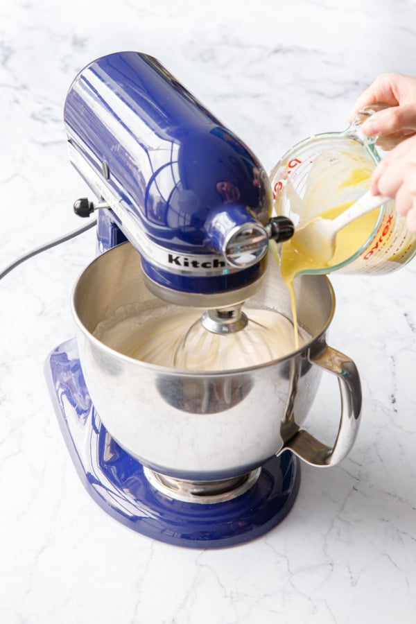 Pouring melted butter and oil mixture into the side of a mixing bowl with the mixer running.