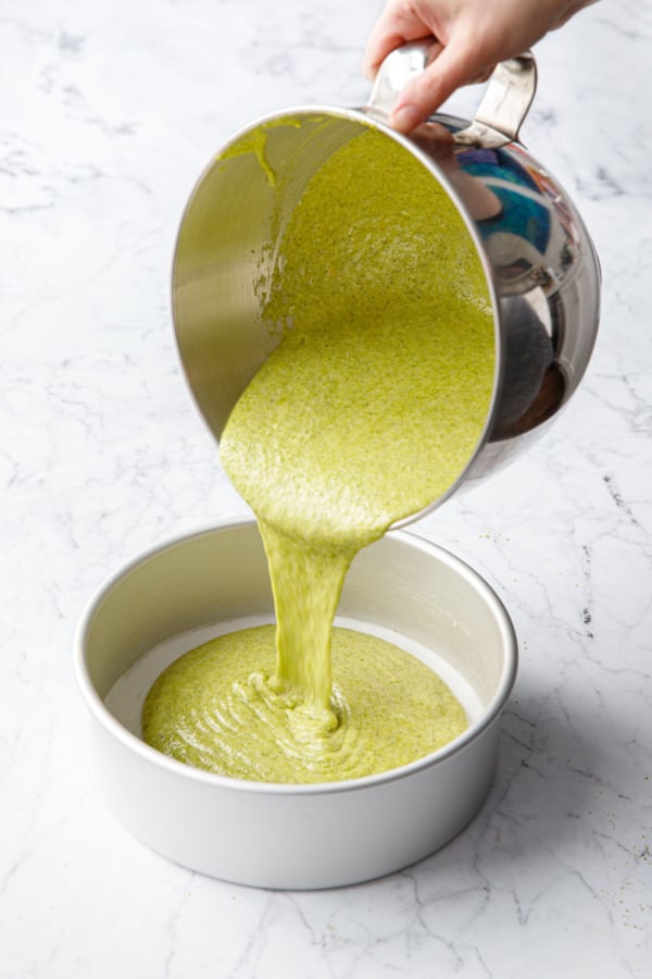 Pouring bright green pistachio cake batter into greased and parchment-lined cake pan.