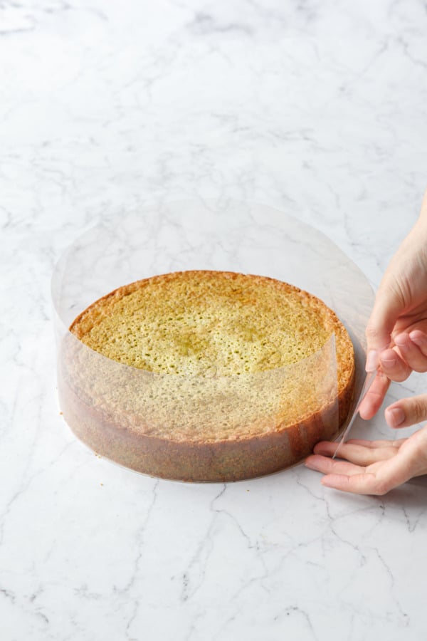 Wrapping a baked and cooled flourless pistachio cake with a strip of 3-inch tall acetate.
