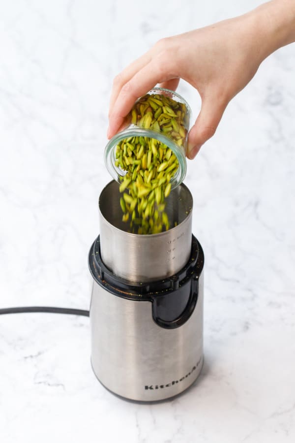 Pouring slivered green pistachios into a coffee grinder to make pistachio flour.