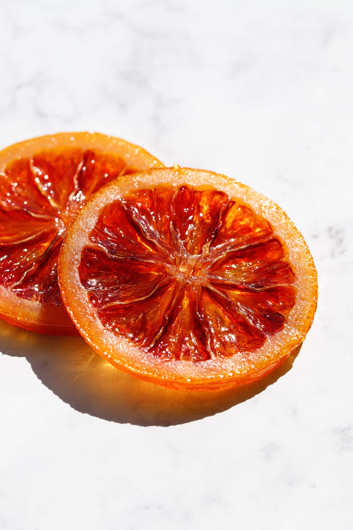 Two slices of Candied Blood Orange Slices in direct light on a marble background.