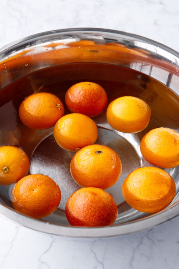 Soaking blood oranges in a large metal bowl filled with hot water to remove any waxy coatings or residue.