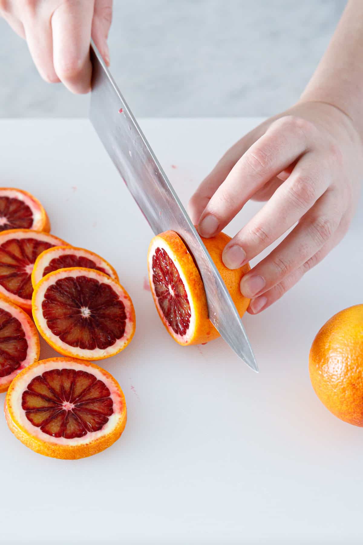 Slicing blood oranges into thin slices for candying.