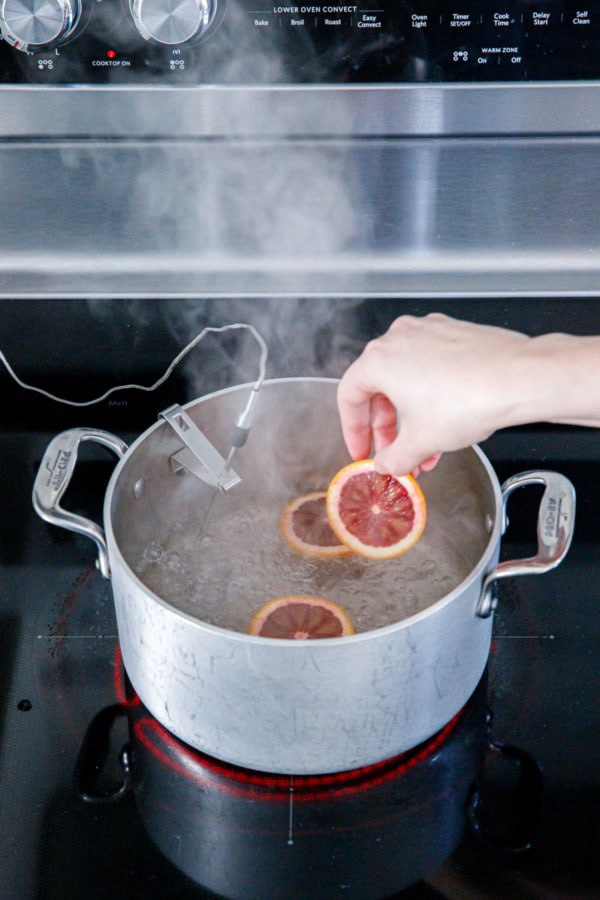 Adding slices of blood oranges into a boiling saucepan with sugar syrup.