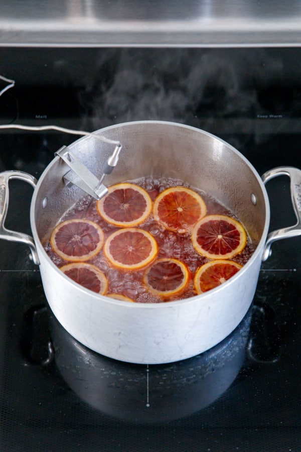 Simmering pot with a red-colored syrup and slices of blood orange.