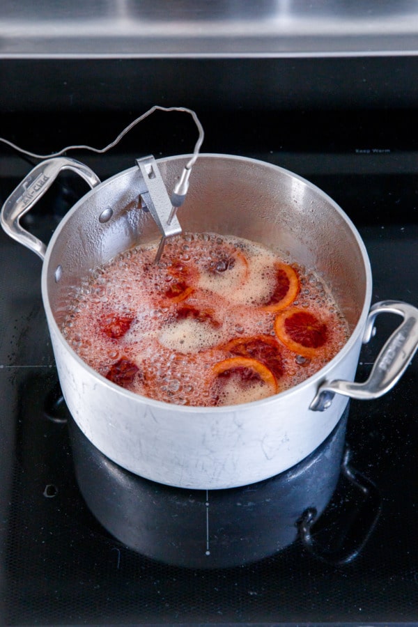 Saucepan with sugar syrup and blood orange slices, bubbling away with a layer of foam.