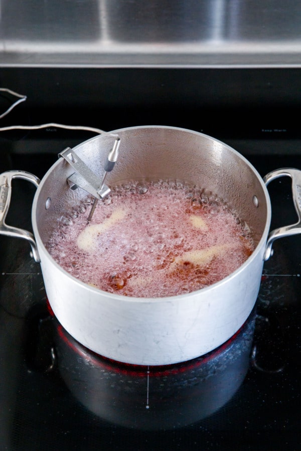 Saucepan filled with a pink-tinted foam, thick enough you can no longer see the orange slices underneath.