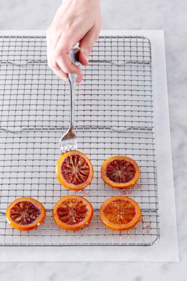 Laying a candied orange slice onto a wire cooling rack sitting on top of a piece of parchment to catch drips.