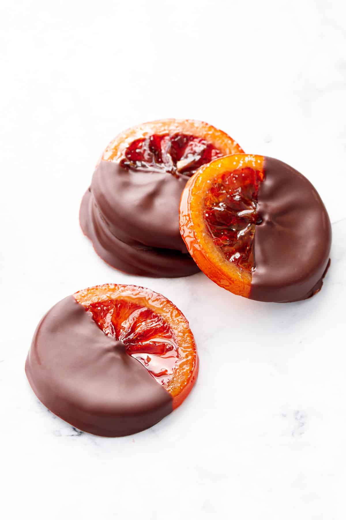 Pile of Candied Blood Orange Slices dipped in dark chocolate, on a marble background.