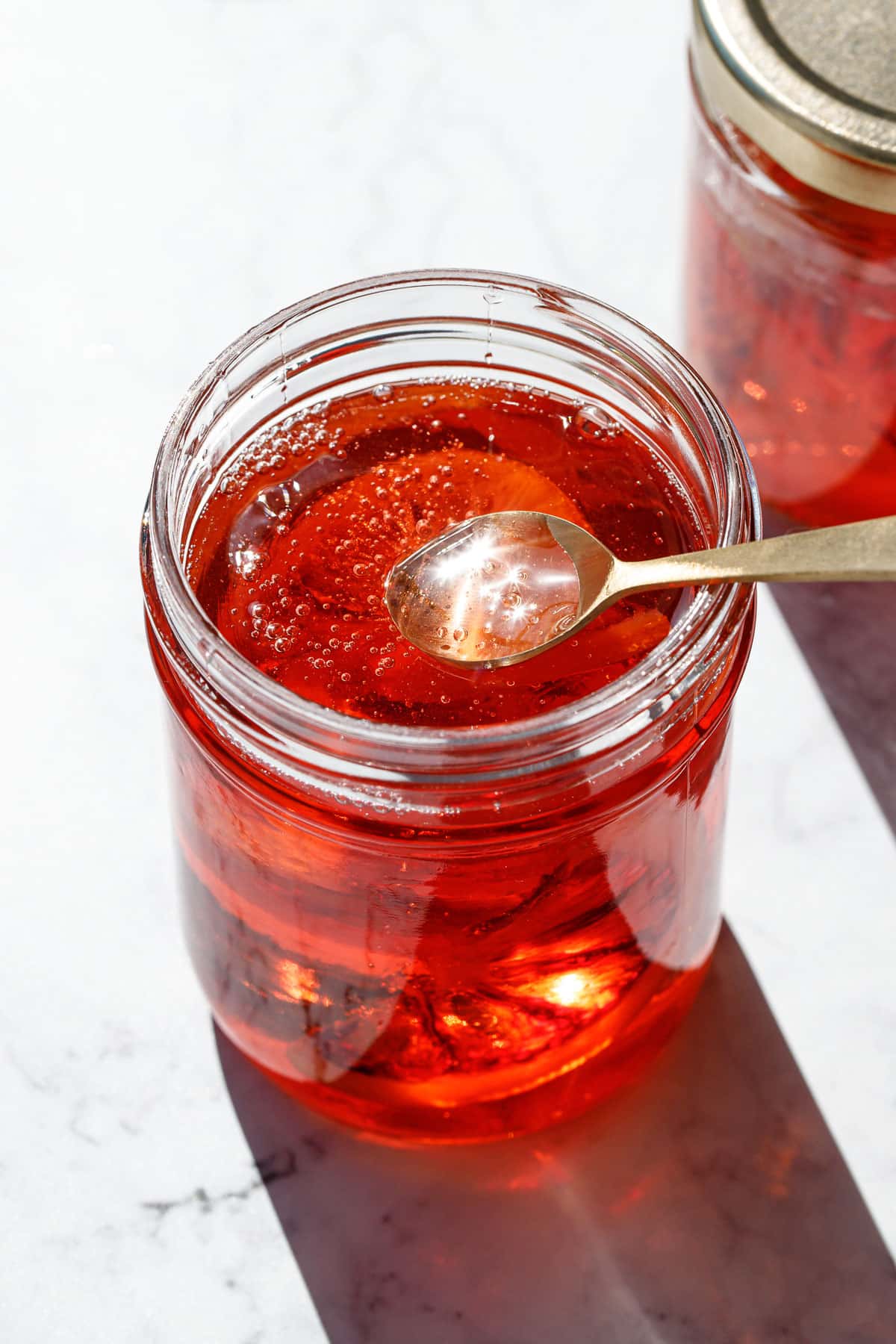 Candied blood orange syrup in a glass jar with a spoon dipping into the jar.