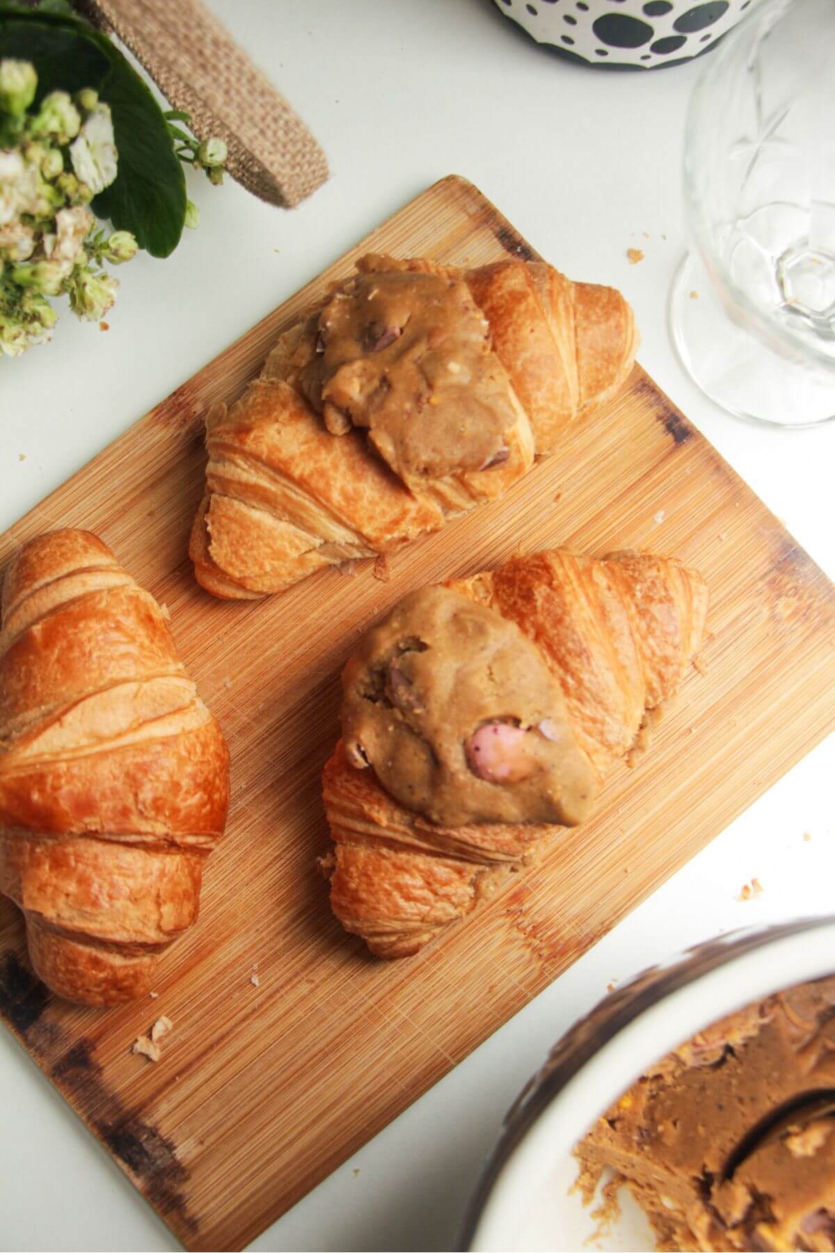 Three croissants on a wooden board, two topped with cookie dough.