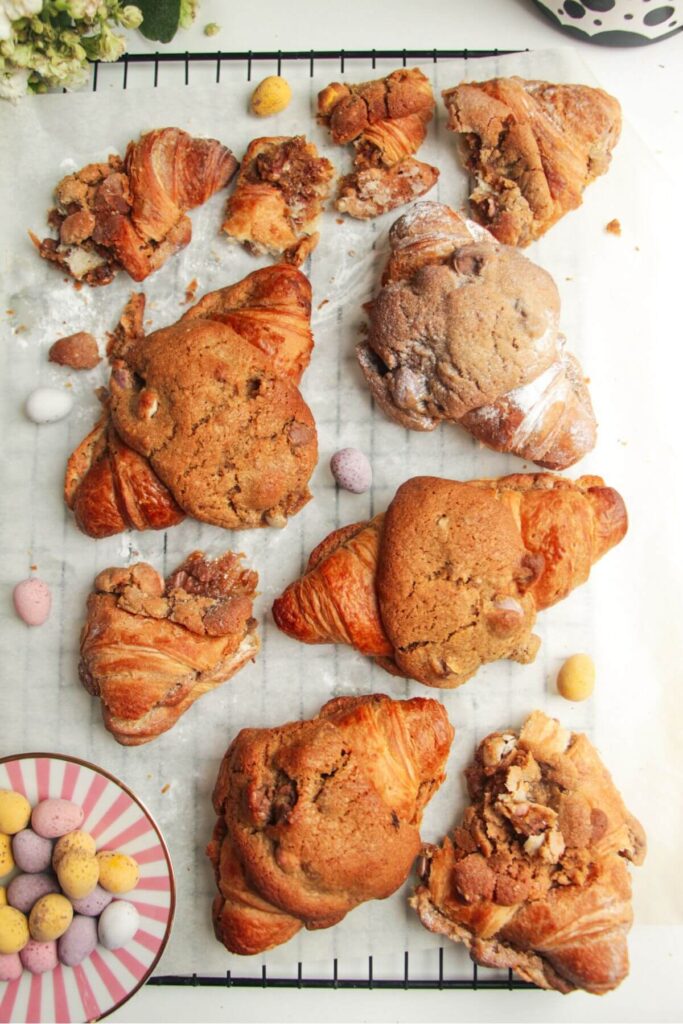 Cookie dough stuffed croissants on a lined baking tray with a coffee cup on the side.