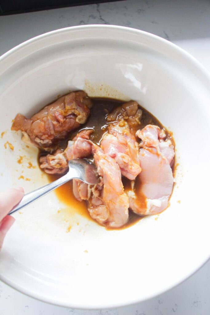 Fork mixing marinade through chicken thighs in a large mixing bowl.