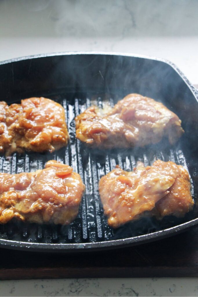 Marinated chicken thighs cooking on a griddle pan.