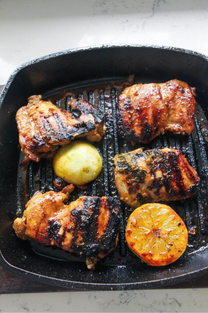 Marinated chicken thighs cooking on a griddle pan with wedges of lemon.