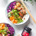 Two baked salmon poke bowls on a marble background with honey on the side.