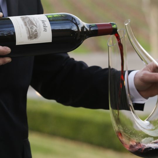 bottle of cabernet magnum pouring wine into glass decanter