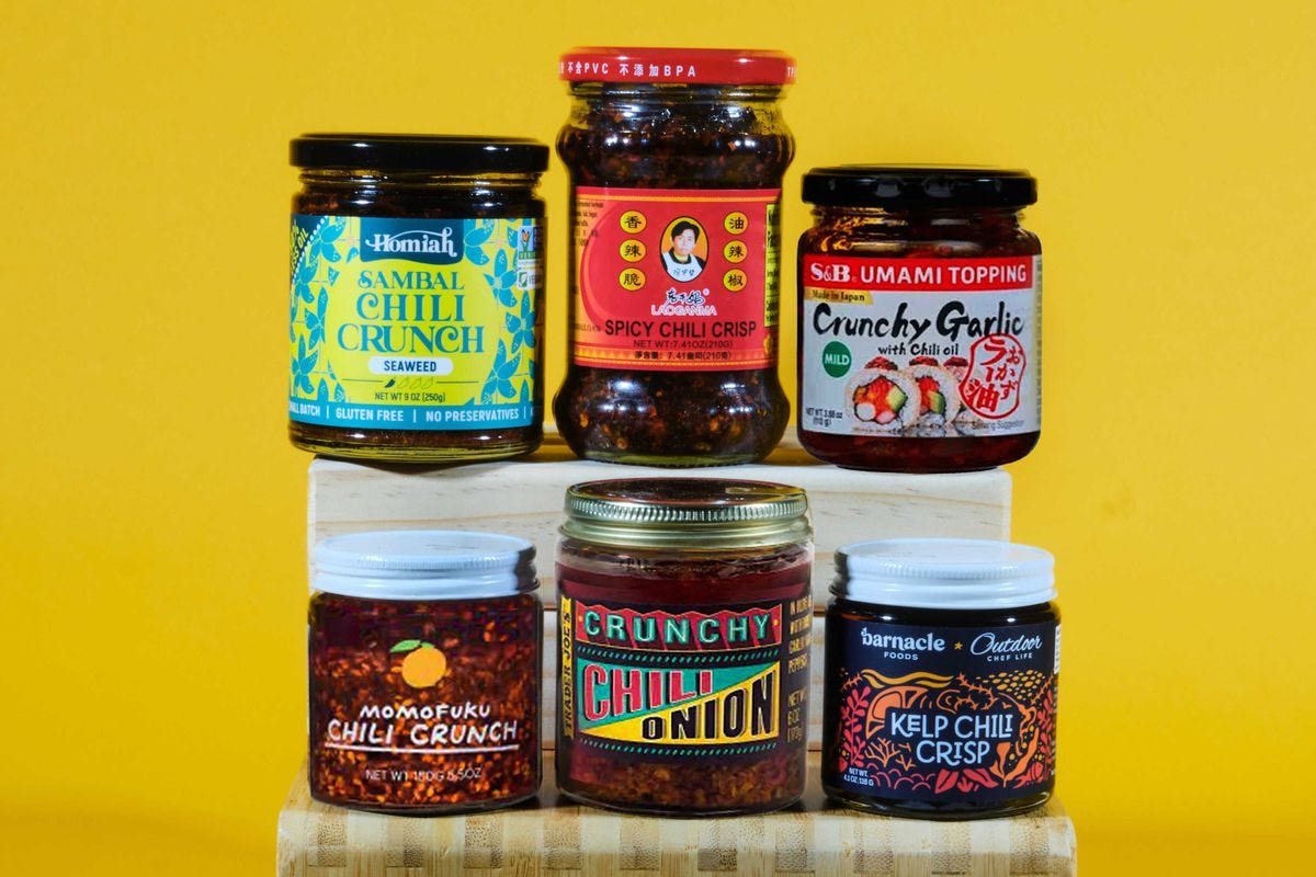 Six glass jars of different sizes and shapes, each containing chile crisp.