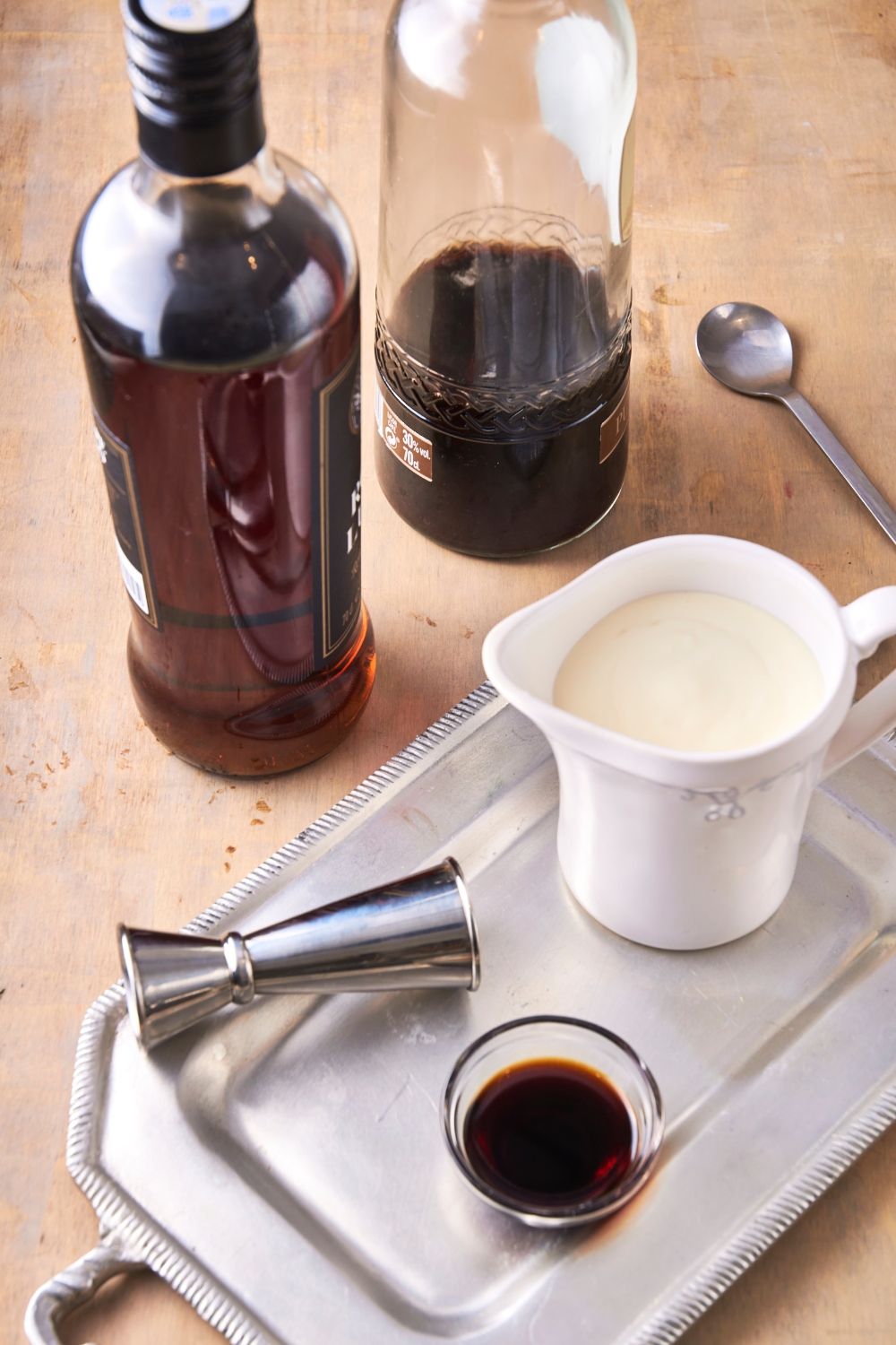 A tray with a pitcher of heavy cream, a small bowl of vanilla extract, a measuring cup, and two bottles of bourbon next to the tray.