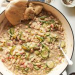 Creamy leek zucchini beans in a large pot with a silver spoon and pita bread on the side.