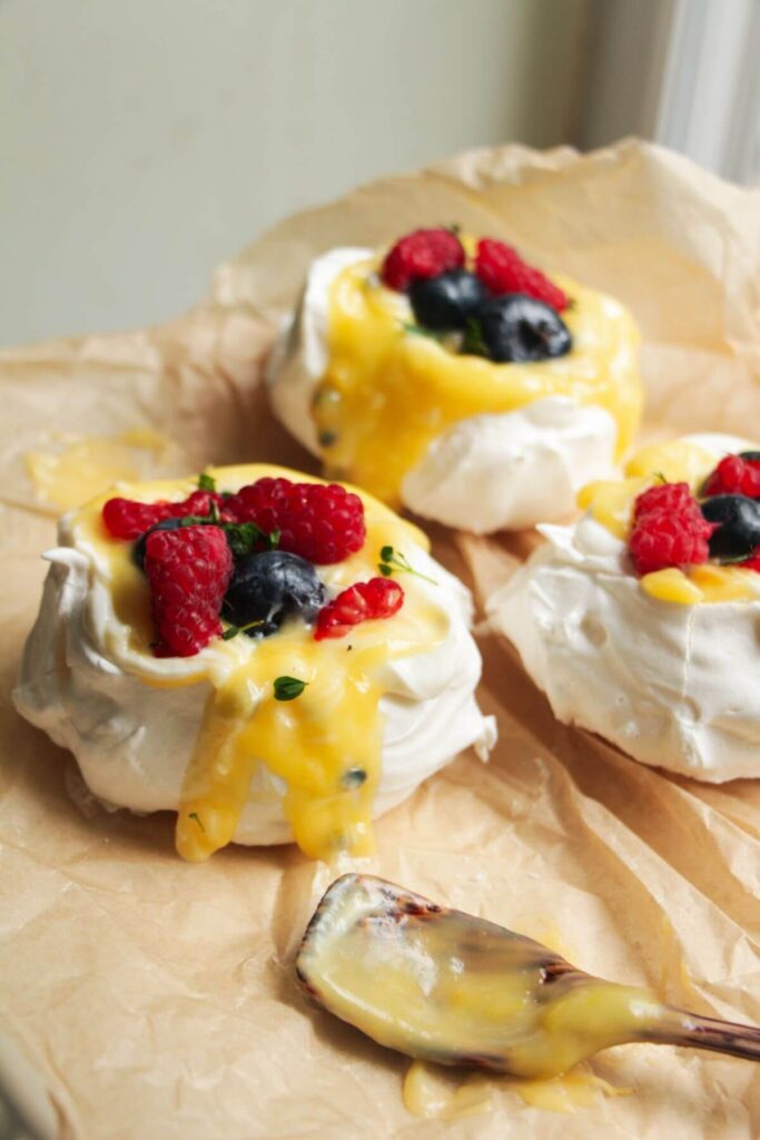Close up of three mini pavlovas, topped with passionfruit curd and berries.