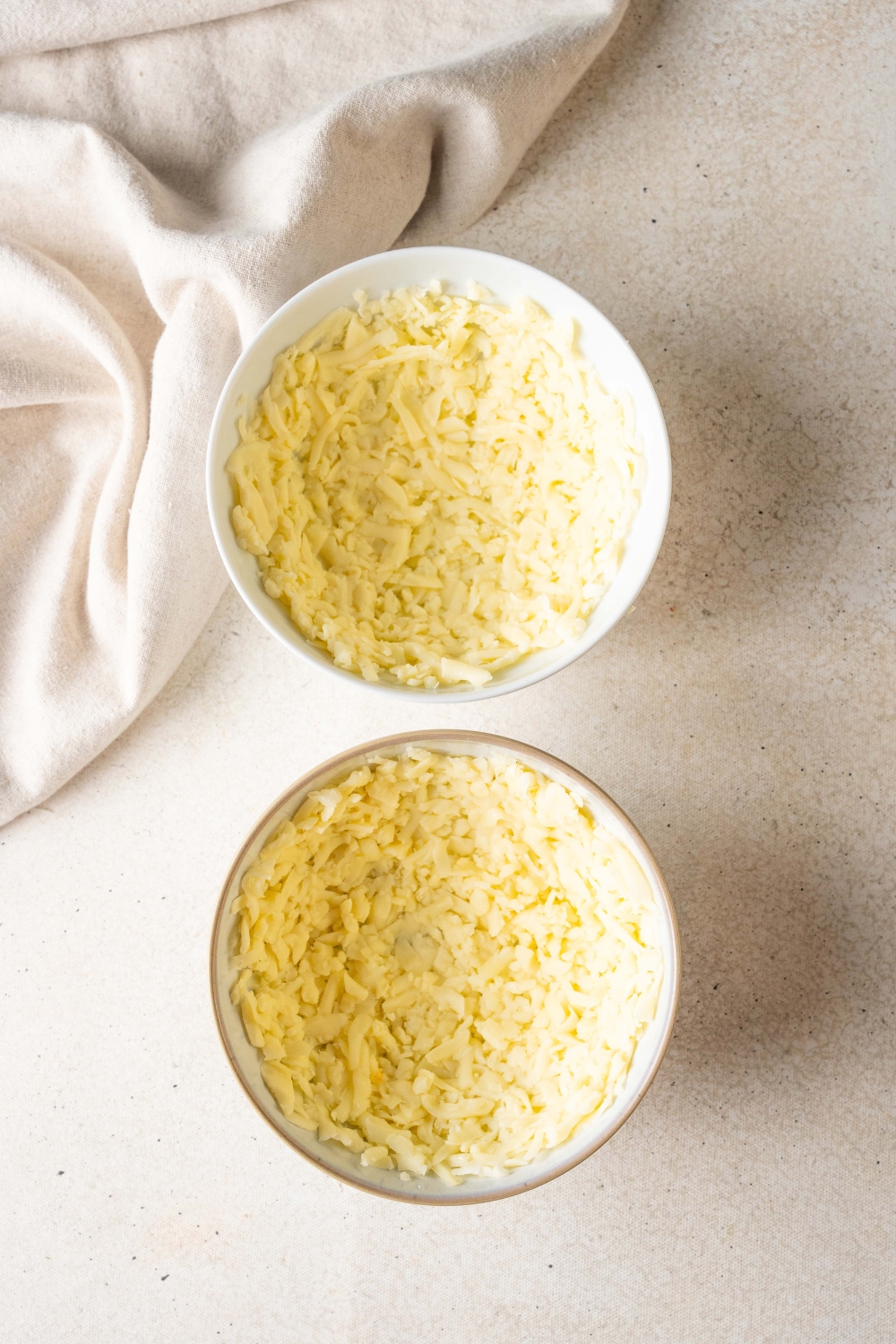 Two bowls are on a counter top. They are filled with grated mozzarella cheese.