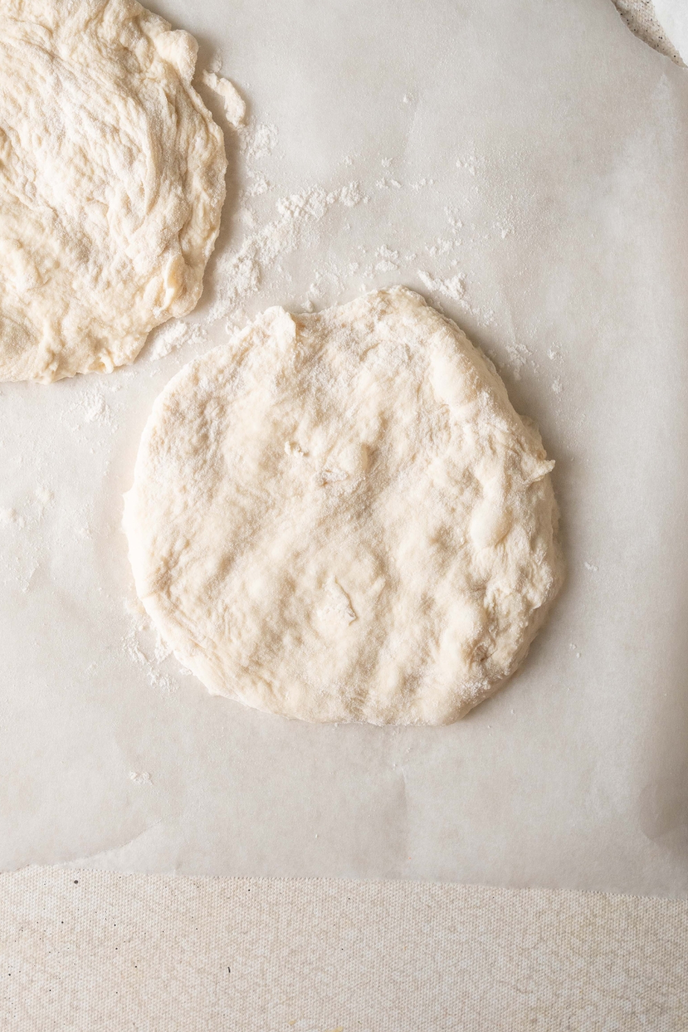 A circle of pizza dough is laying on a piece of parchment paper. There is flour dusted around it.