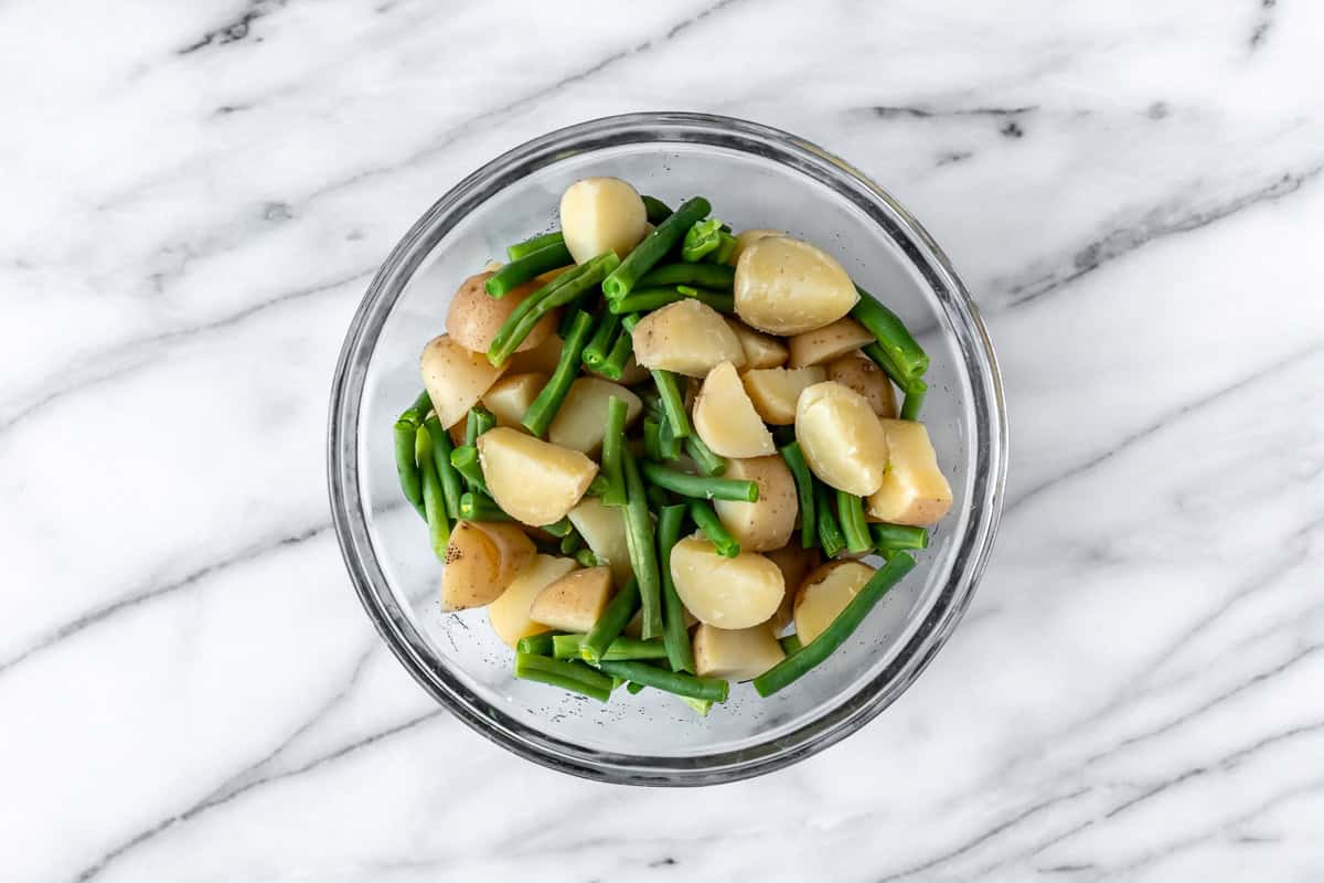 Potatoes and green beans in a glass bowl over a marble background.