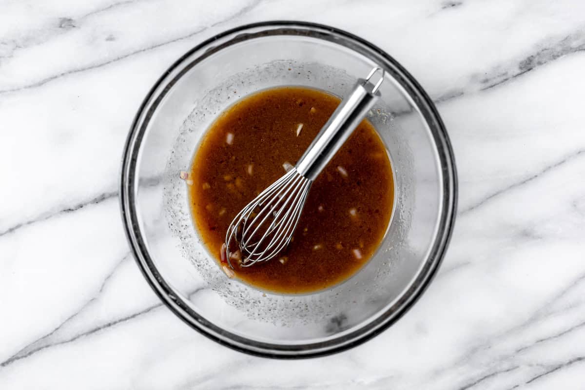 Brown dressing in a glass bowl with a whisk over a marble background.