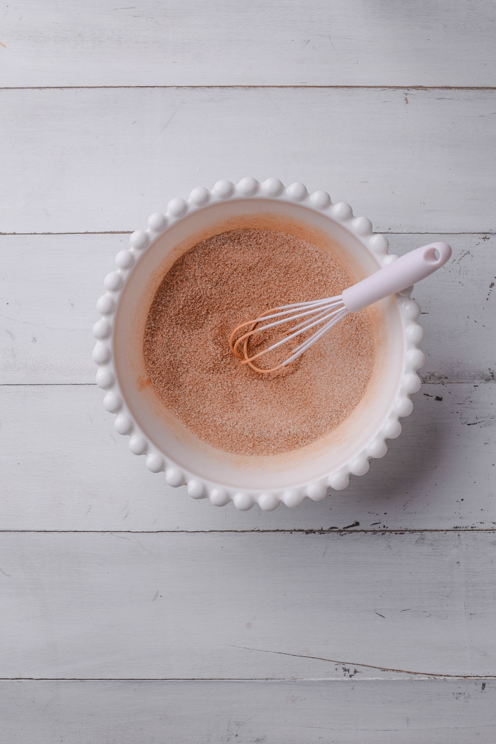 A white bowl holds the cinnamon and sugar mixture. A white whisk rests in the bowl, also.