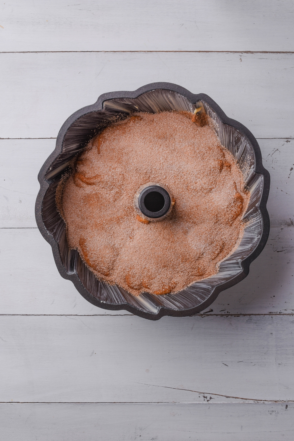 A black bundt cake pan holds half of the cinnamon bundt cake mixture. The cinnamon sugar mixture has been sprinkled on the top.
