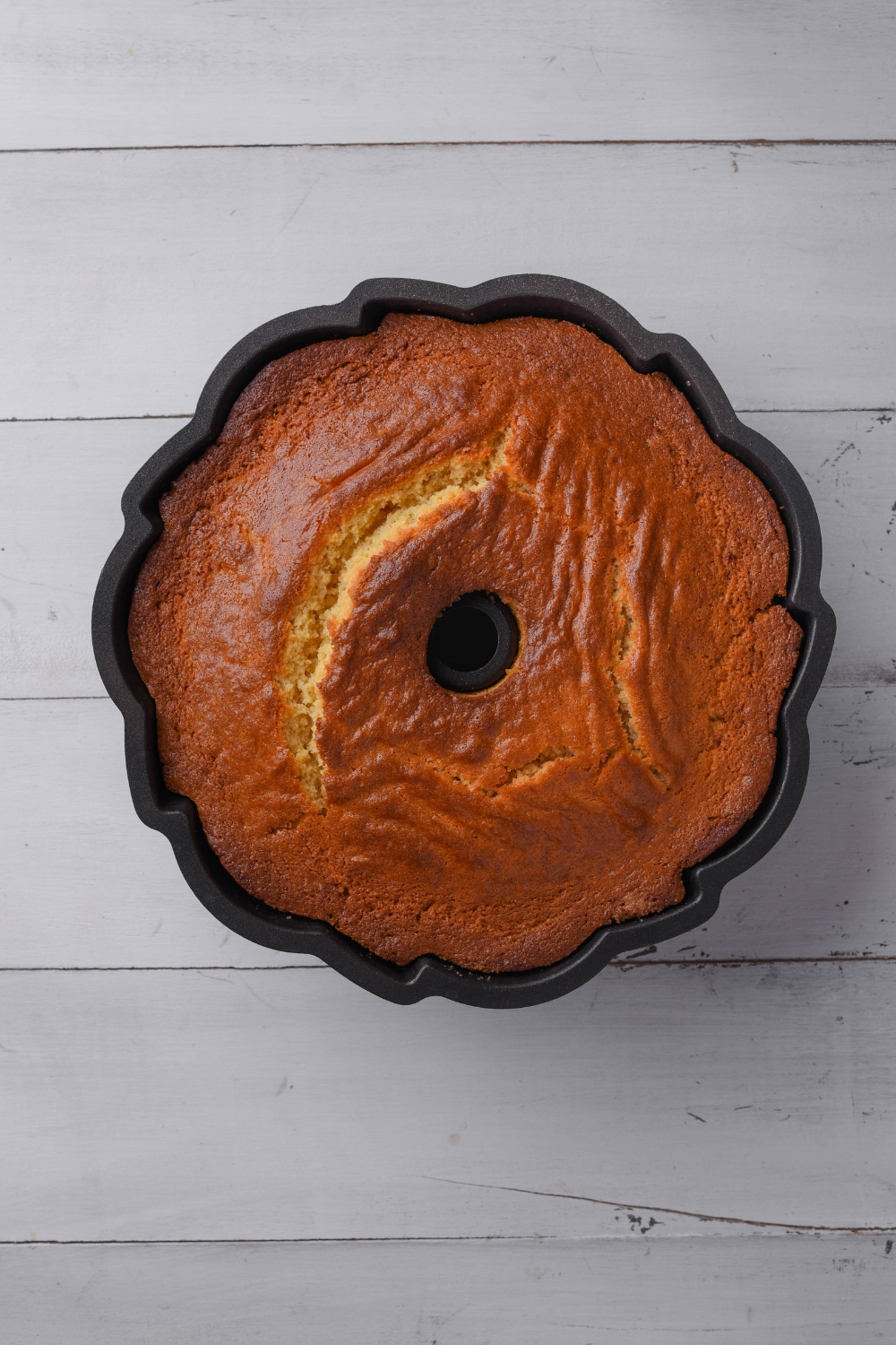 A golden brown cinnamon bundt cake cools in a black bundt pan.