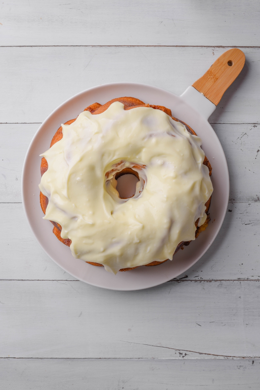 A frosted cinnamon bundt cake sits on a white and wooden serving platter.