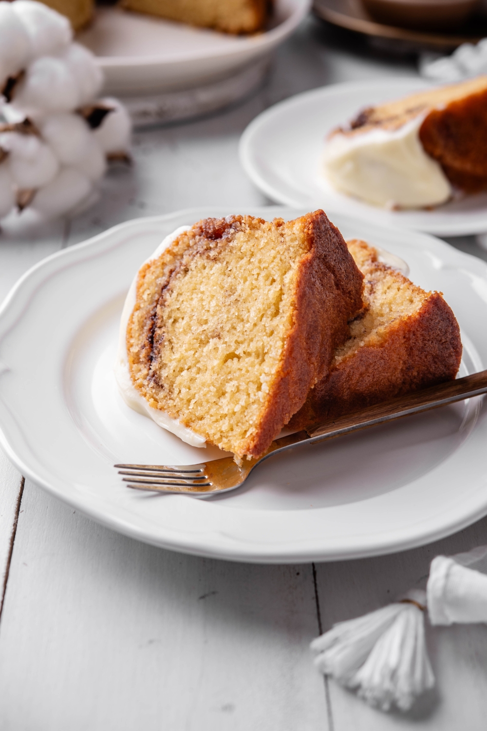 Two slices of cinnamon bundt cake rest on a white plate. There is a fork nearby.